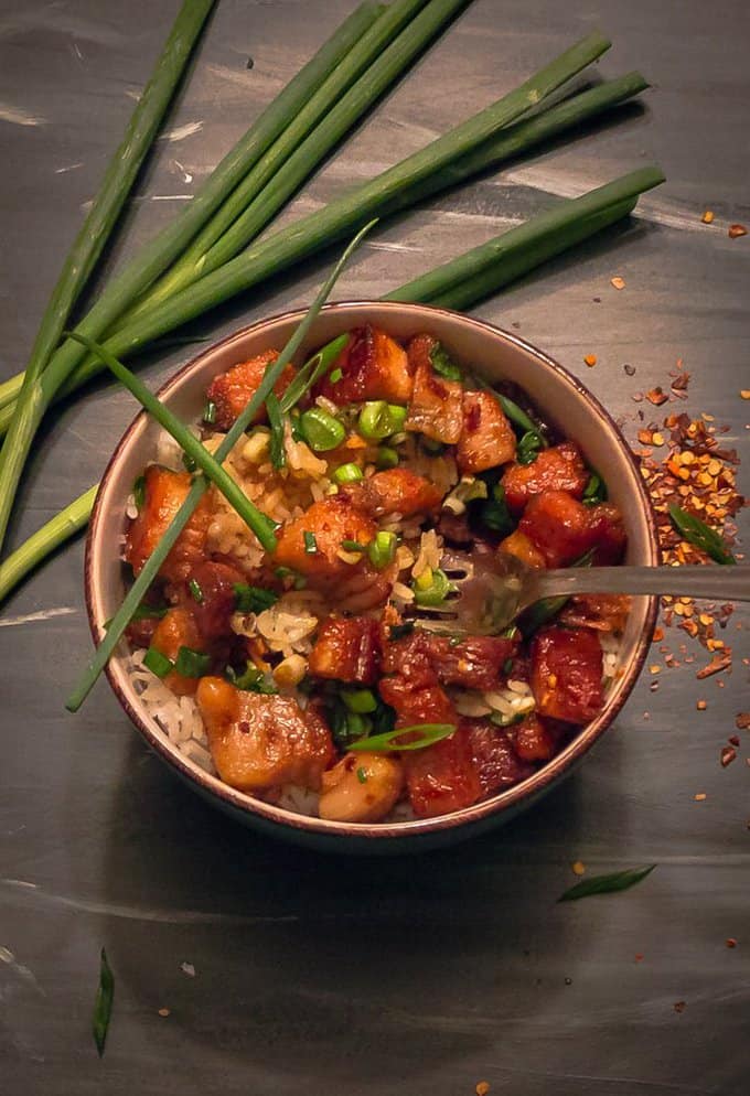 Sticky Chinese Pork Belly in bowl with a green onion garnish on back background