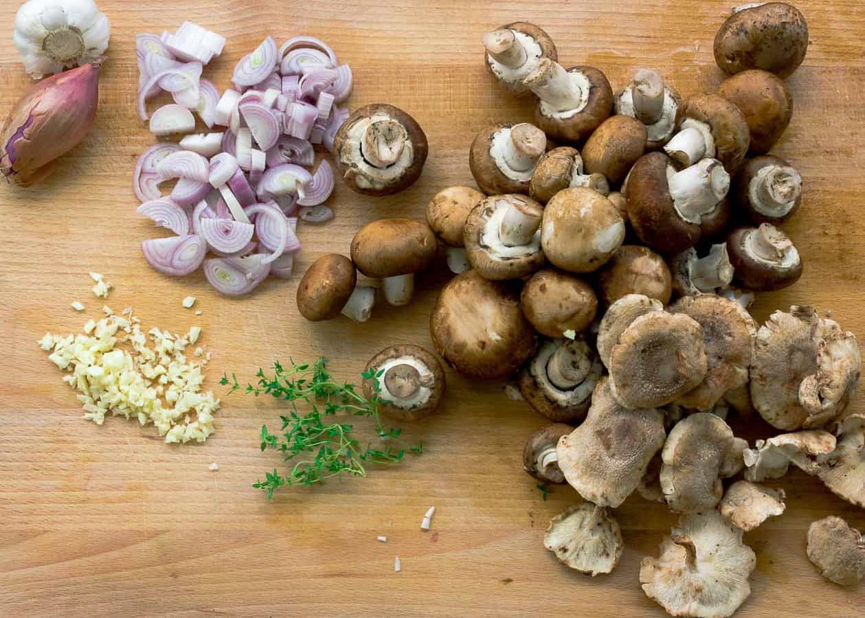 Prepping for Crispy Roasted Chicken with Mushrooms and Cream. Cutting board with shallots, garlic, mushrooms, and thyme being sliced.