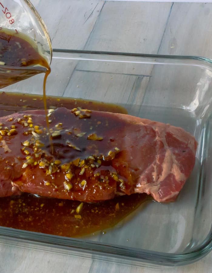 The best teriyaki marinade shown poured from a glass measure cup onto a speak.