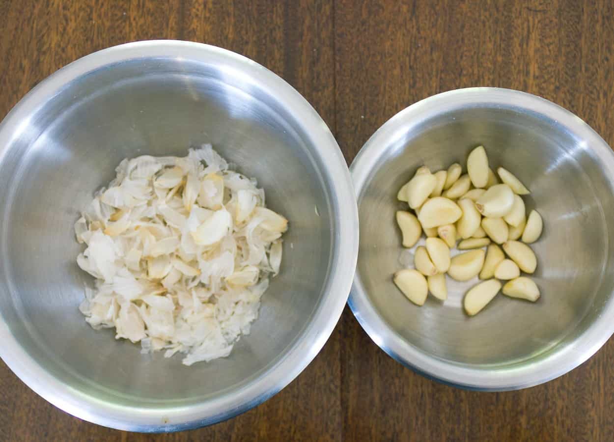 two metal bowls, one with peeled garlic cloves and one with peels
