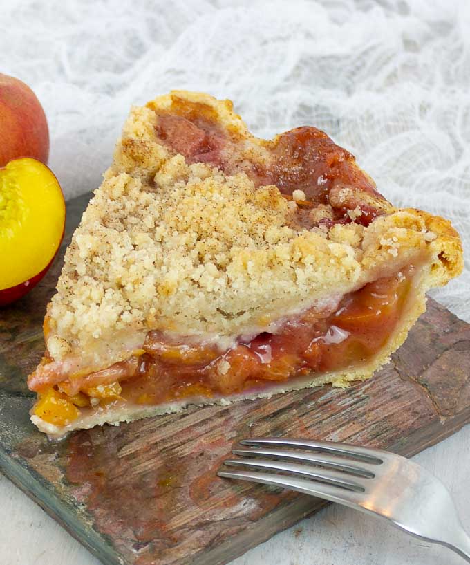 one slice of Fresh Peach Pie With Crumb Topping and the tines of a fork
