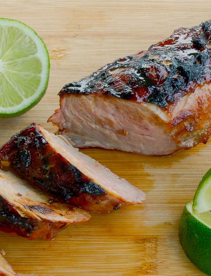 Smokey Brown Sugar Crusted Pork Tenderloin sliced on bamboo cutting board with lime wedges