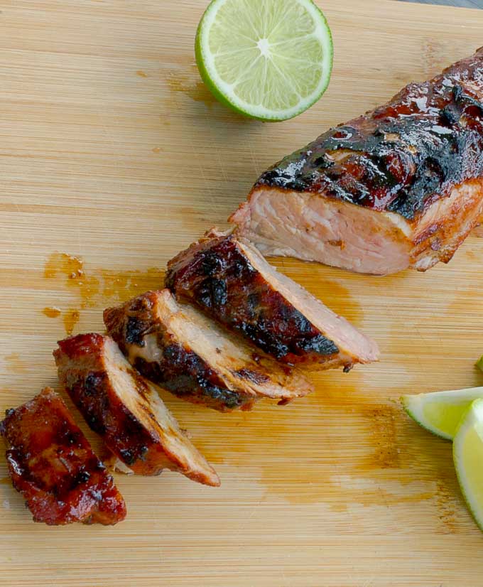 Smokey Brown Sugar Crusted Pork Tenderloin sliced on bamboo cutting board with lime wedges