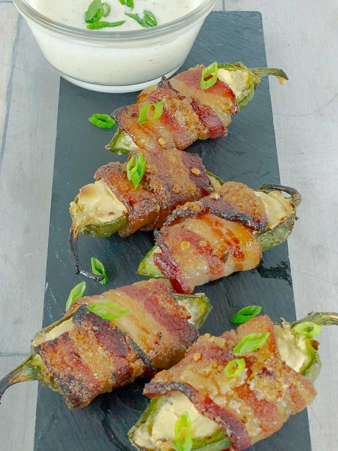 five Bourbon Candied Bacon Wrapped Jalapeno Poppers on a piece of slate with ranch