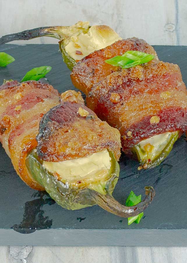 two Bourbon Candied Bacon Wrapped Jalapeno Poppers on black slate