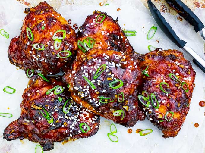five pieces of Sticky Asian Grilled Chicken Thighs on white background with tongs