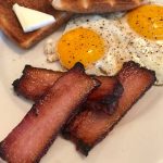 Home Cured Hickory Smoked Bacon on white plate with eggs