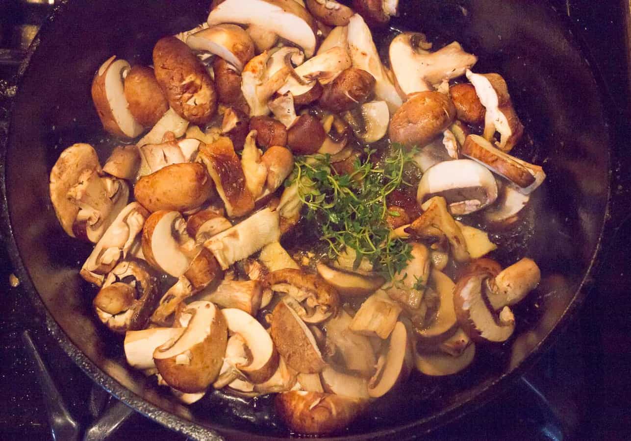 Mixed types of sliced mushrooms are browned in olive oil and butter with thyme sprigs, salt, pepper.