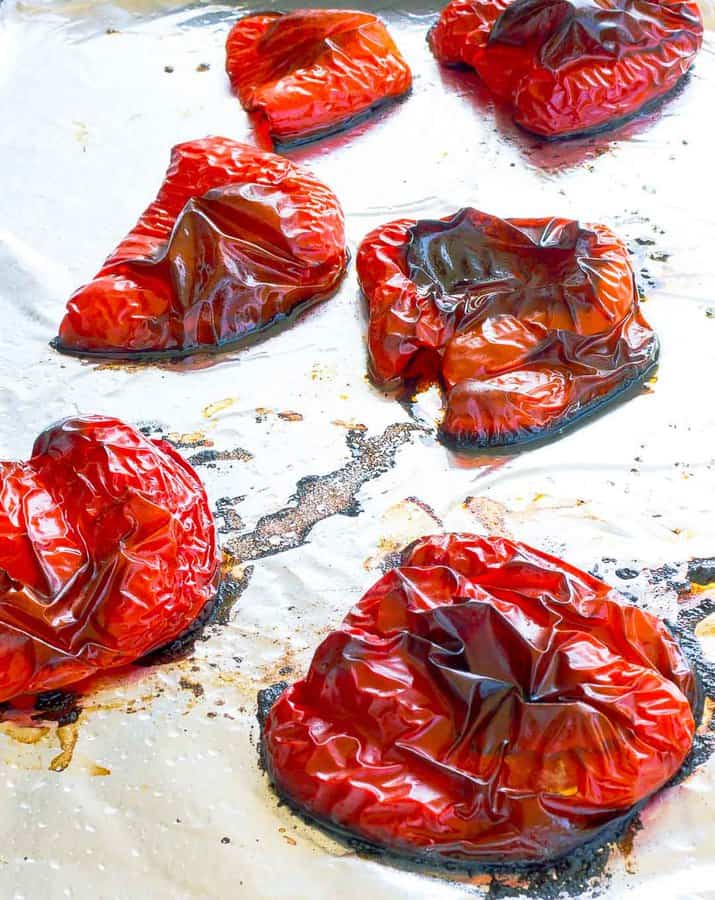 Six roastes red pepper halves on a foil lined cookie sheet