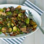 Roasted Brussels Sprouts with Bacon and Shallots on white oval dish on whitewashed plank background