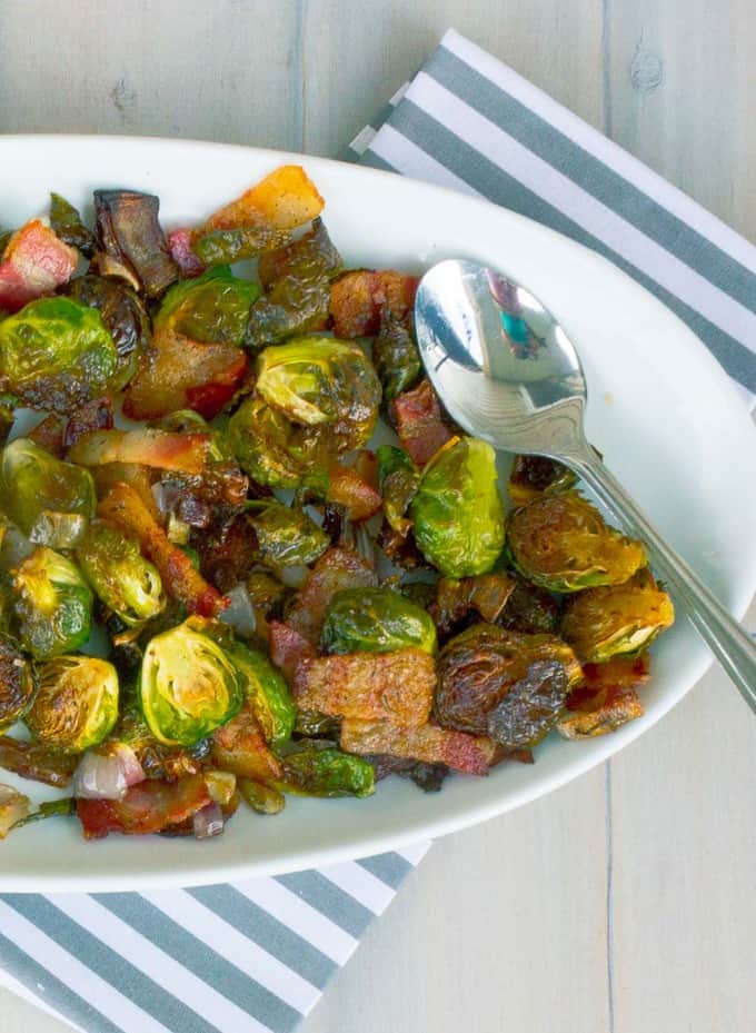 Roasted Brussels Sprouts with Bacon and Shallots on right side of a white oval dish on whitewashed plank background