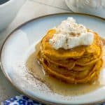 side view of Pumpkin Pie Pancakes With Spiced Whipped Cream with whipped cream and syrup on the side