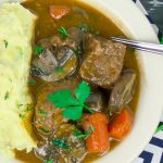 Beef and Guinness Stew in white bowl with mashed potatoes