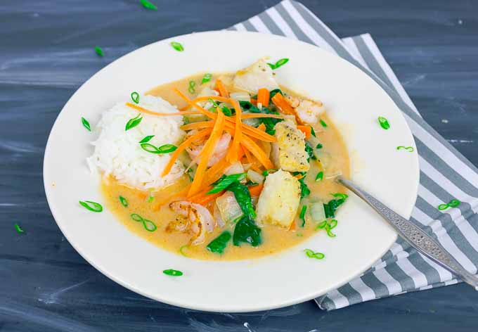 Thai Red Curry with Fish and Shrimp in white bowl with rice and green onion garnish