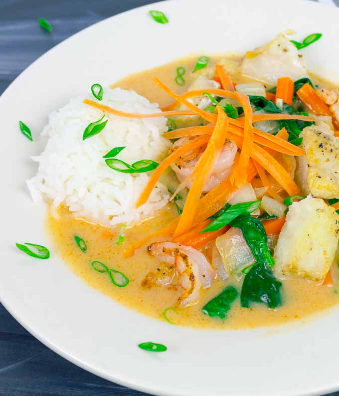 Thai Red Curry with Fish and Shrimp in white bowl with rice and green onion garnish