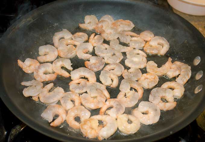 raw shrimp being cooked in a fry pan for shrimp alfredo
