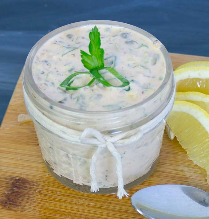 Spicy Remoulade Sauce in glass jar on wood cutting board with parsly, green onion, and lemon