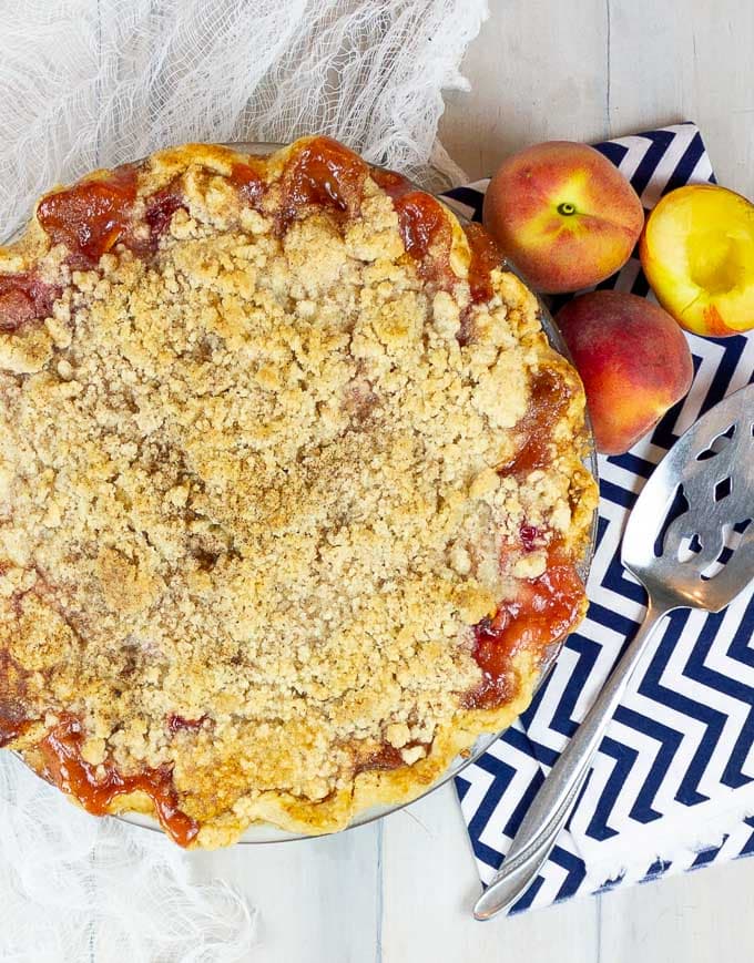 Fresh Peach Pie With Crumb Topping with whole peaches and a serving tool