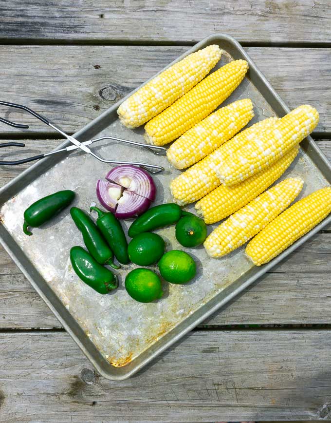 fresh corn, limes, jalepenos, and red onion on a metal pan