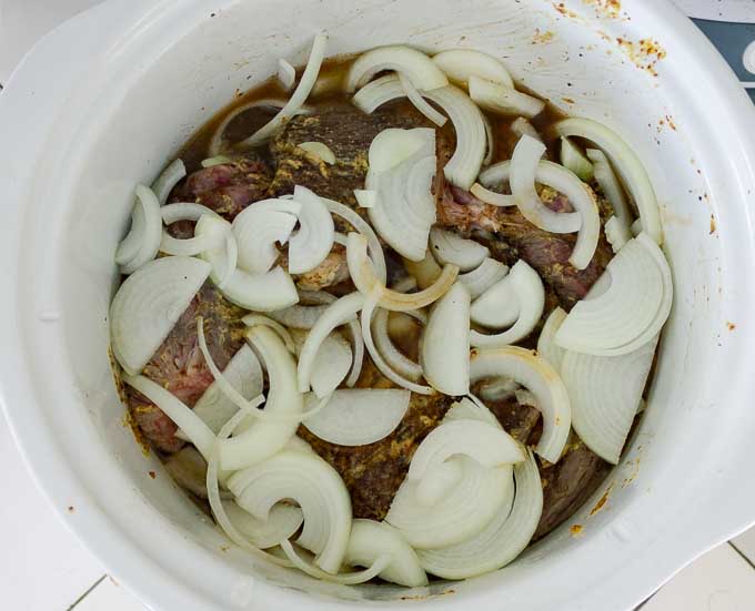 Sliced white onions and au jus around roast in crock pot.