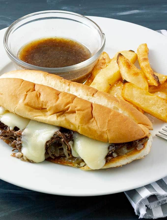 Crockpot French Dip Sandwich Recipe on white plate with fries and au jus.