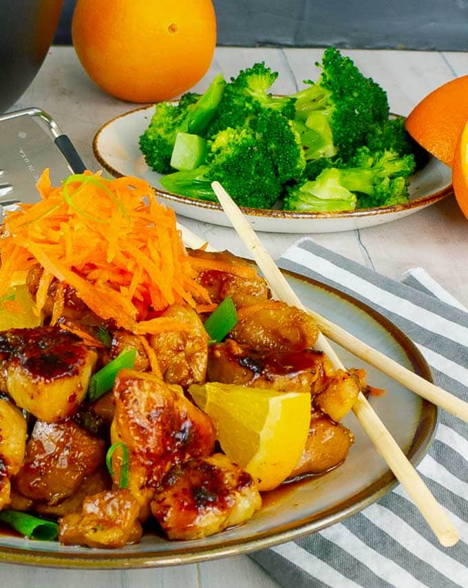 plate of sticky orange chicken with broccoli in the background