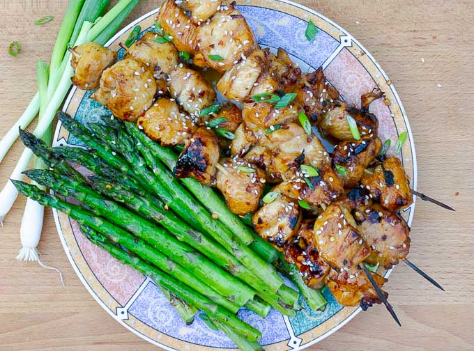 four Grilled Asian Chicken Kabobs on a plate with grilled asparagus