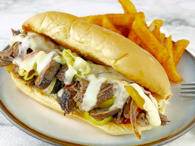 Crockpot Philly Cheesesteak sandwich on white plate with dark rim and fries