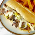Slow cooker Philly cheese steak sandwich on white plate with fries
