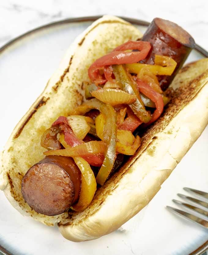 a Sheet Pan Polish Sausage Sandwich on a white plate with onions and peppers