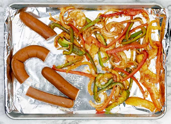 sausage pieces and onions and peppers on a cookie sheet