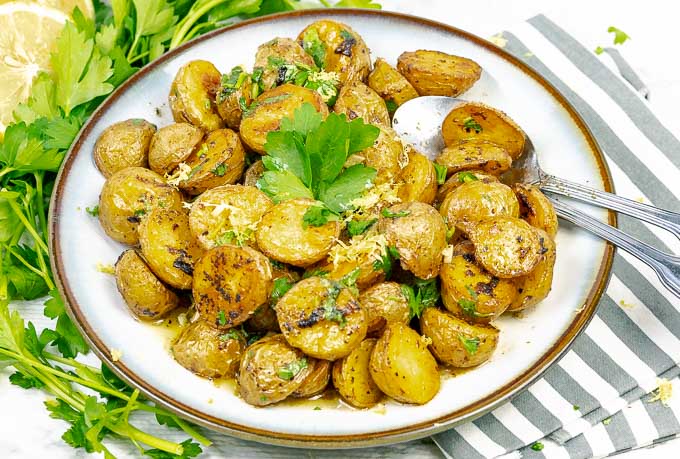 Roasted Lemon Parsley Butter Potatoes on white plate with parsley and lemon slices