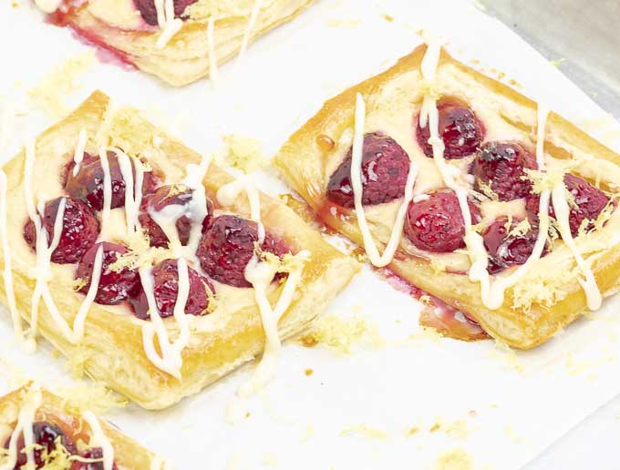 two raspberry puff pastry tarts with lemon cream cheese on a baking sheet