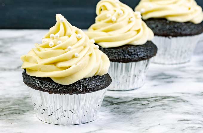 three Guinness Dark Chocolate Cupcakes with Irish Cream Cream Cheese Frosting in silver wrappers