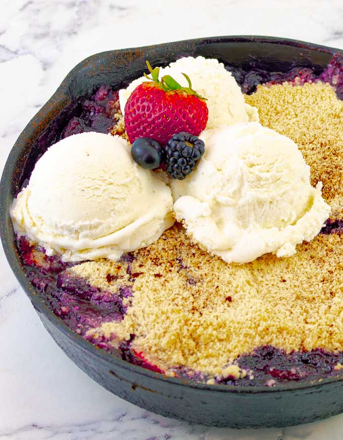 Grilled Triple Berry Crisp in a Cast Iron Skillet with three scoops of ice cream and berries