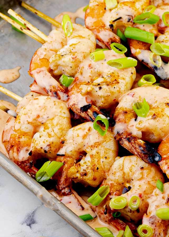 Grilled Bang Bang Shrimp skewers on metal tray with green onion slices