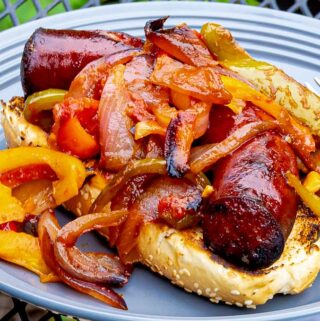 Grilled Sausage with Peppers and Onions on a bun on a gray plate