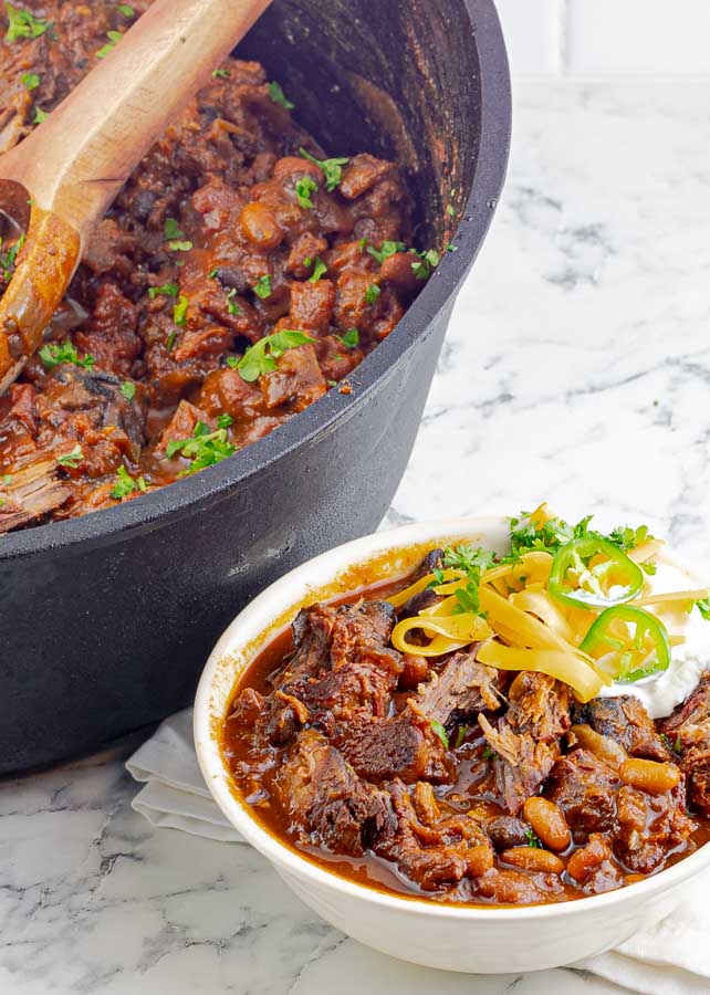 white bowl of smoked chuck roast chili with sour cream and cheese