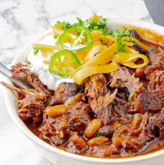 white bowl of smoked chuck roast chili with sour cream and cheese