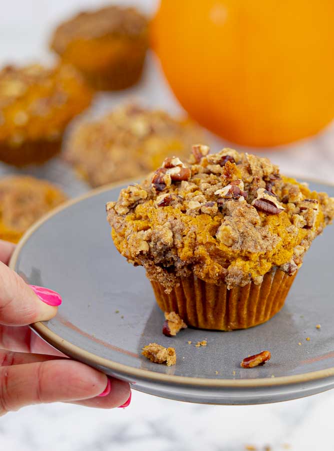 an Easy Pumpkin Muffins with Pecan Streusel on gray plate being held by a hand