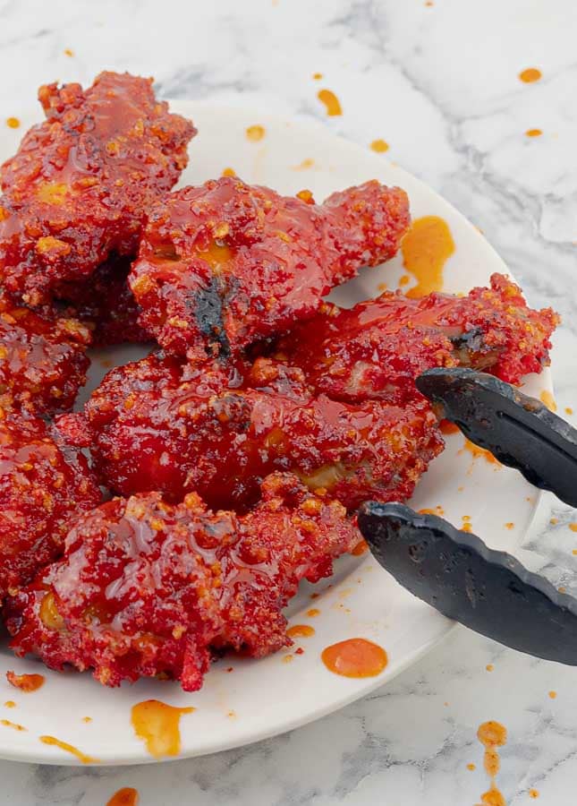 white place of Flamin' Hot Cheetos Wings with Honey Sriracha Sauce with tongs