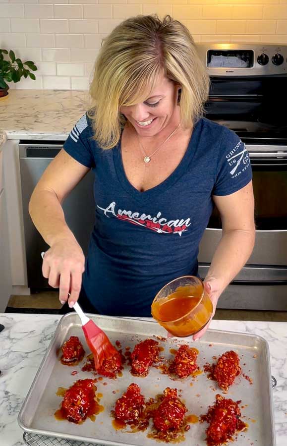 Jennifer saucing a baking sheet of Flamin' Hot Cheetos Wings with Honey Sriracha Sauce