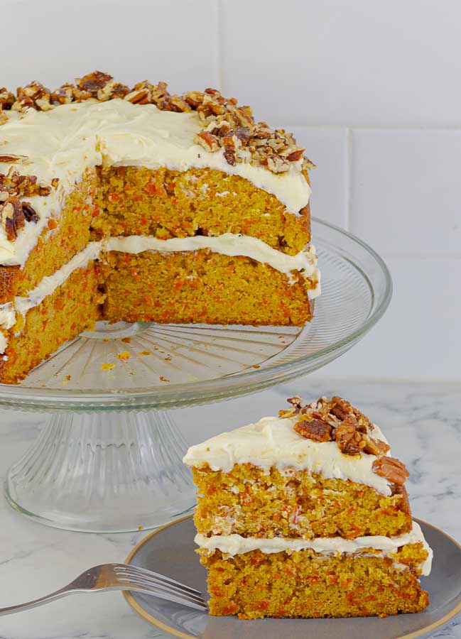 classic carrot cake recipe with cream cheese icing slice on a gray plate with the rest in the background