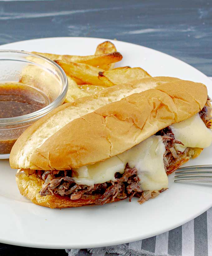Crockpot French Dip Sandwich on white plate with au jus and French fries