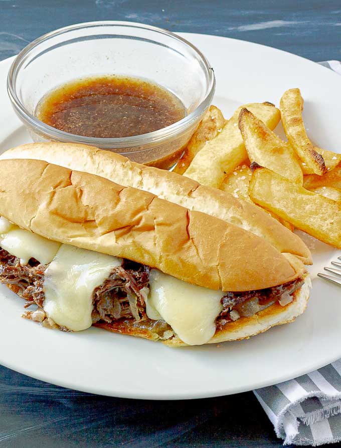 Crockpot French Dip Sandwich on white plate with au jus and French fries