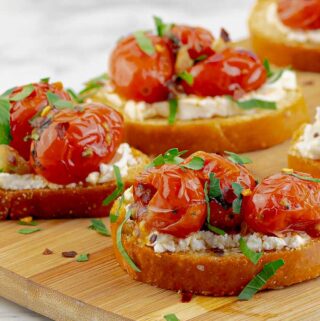 close up of goat cheese crostini with blistered tomatoes on cutting board