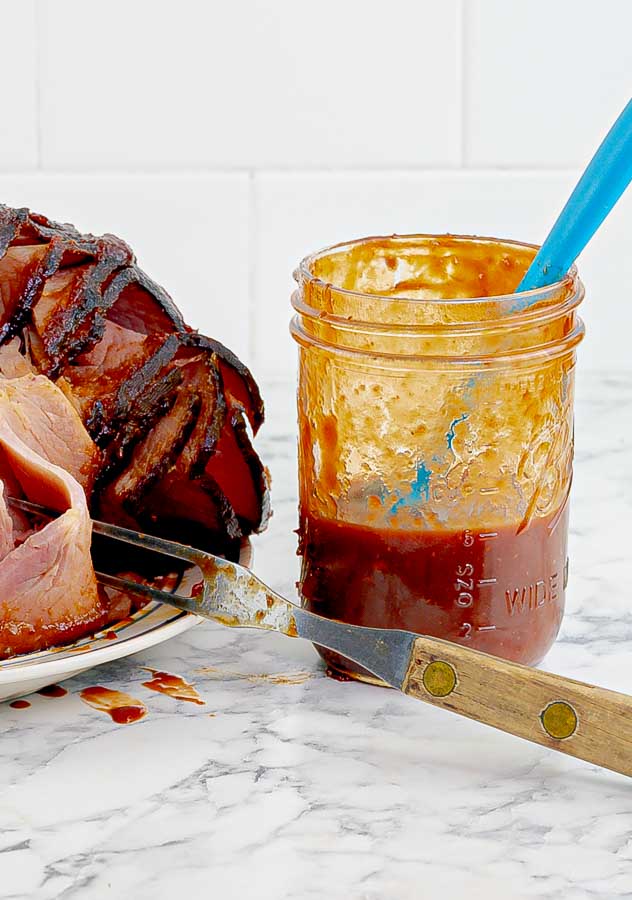 half empty jar of cranberry chipotle barbecue sauce next to a ham