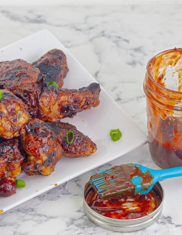 barbecue chicken wings on a white plate with a jar of sauce