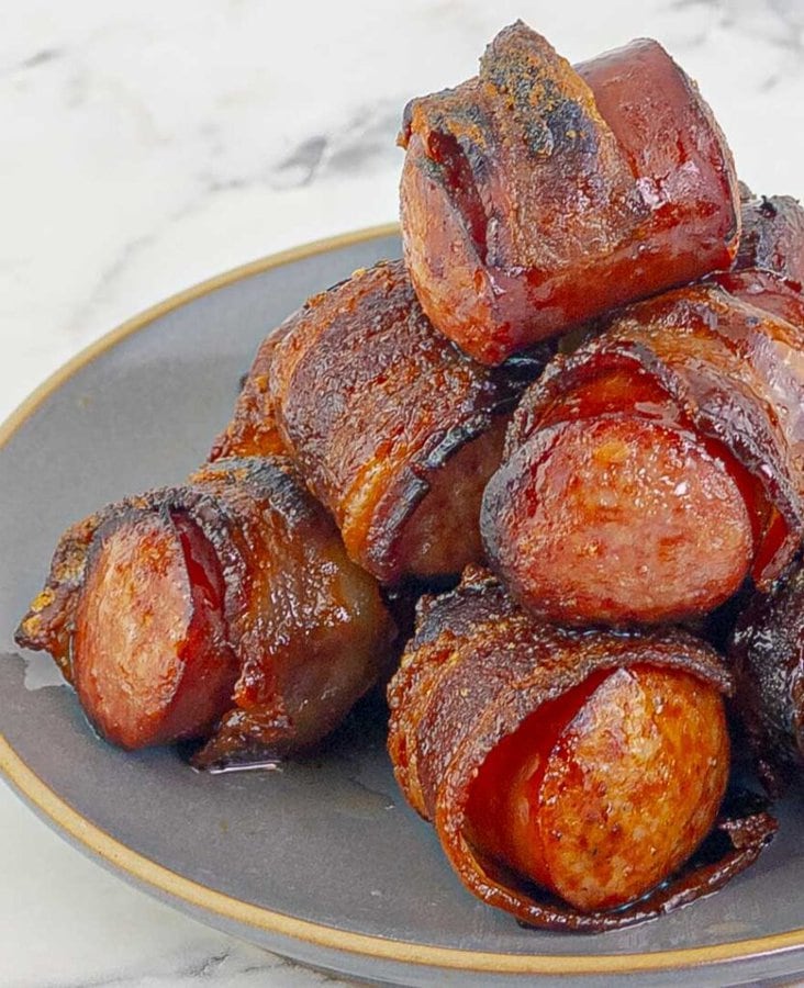 Bourbon Brown Sugar Bacon Wrapped Sausages stacked on top of each other on a gray plate