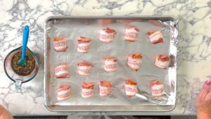 sausages wrapped in bacon on a foil lines baking sheet